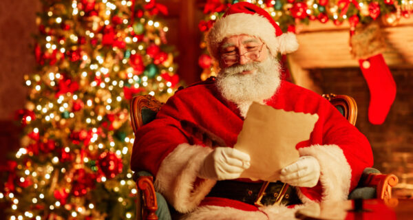Portrait of traditional Santa Claus reading letter by fireplace on Christmas eve and smiling, copy space